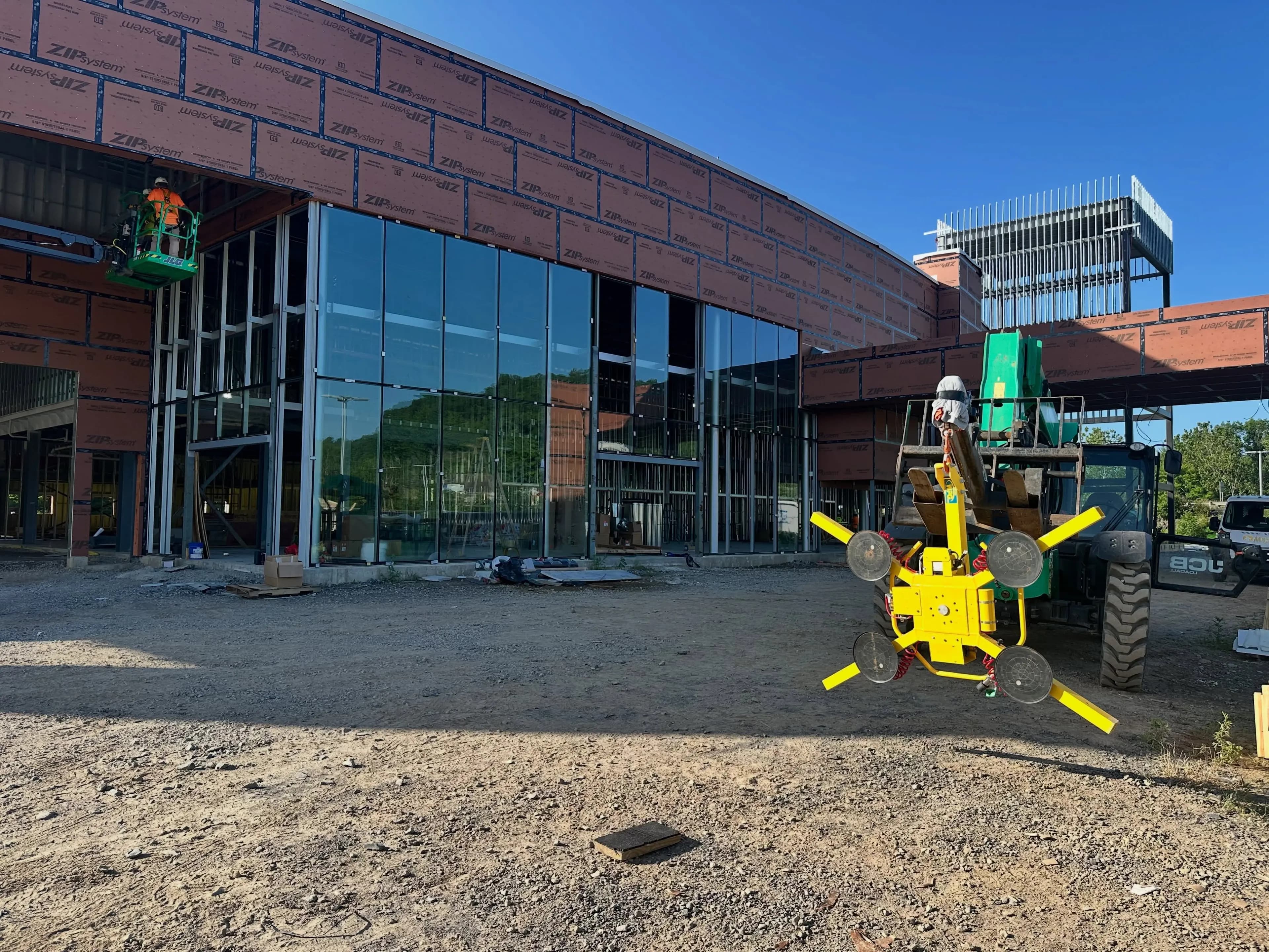 Curtain-wall glass being set on a commercial building with a vacuum lifter on a telehandler