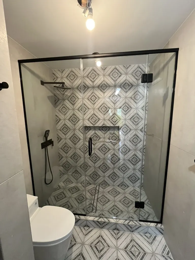 Black-framed sliding shower door against bold geometric encaustic tile and microcement walls.
